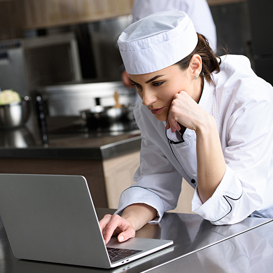 Female chef looking up a recipe on a laptop